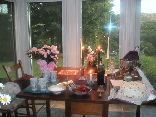 sunroom with table set with flowers, strawberries, cake, candles, champaign bucket